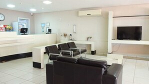 A modern waiting area with a reception desk, a sofa, a TV, and a coffee machine. - Vilhar Palace Hotel (Ivaipora)