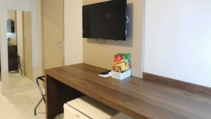 A room with a wooden desk, a television mounted on the wall, and a small refrigerator. - Vilhar Palace Hotel (Ivaipora)