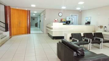 A reception area with a counter, chairs, a clock, and a staircase leading to another room.