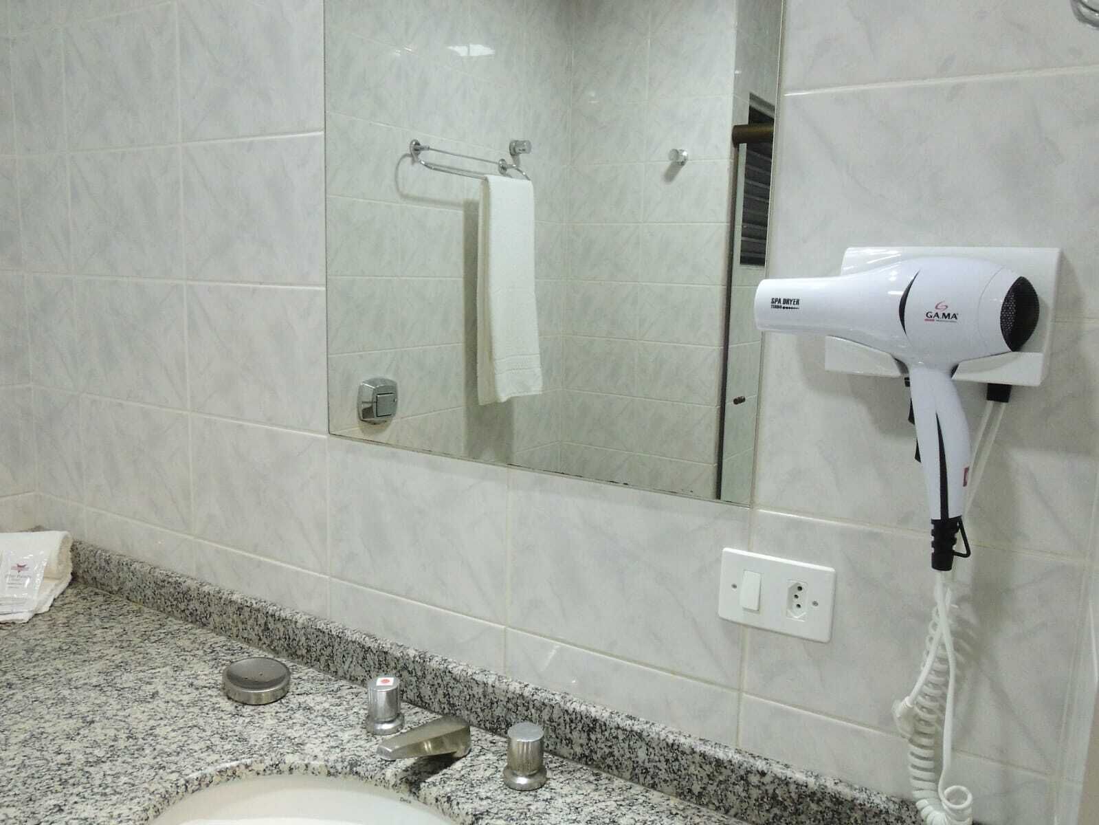 A bathroom with a marble countertop, a sink, a hair dryer mounted on the wall, and a towel rack.