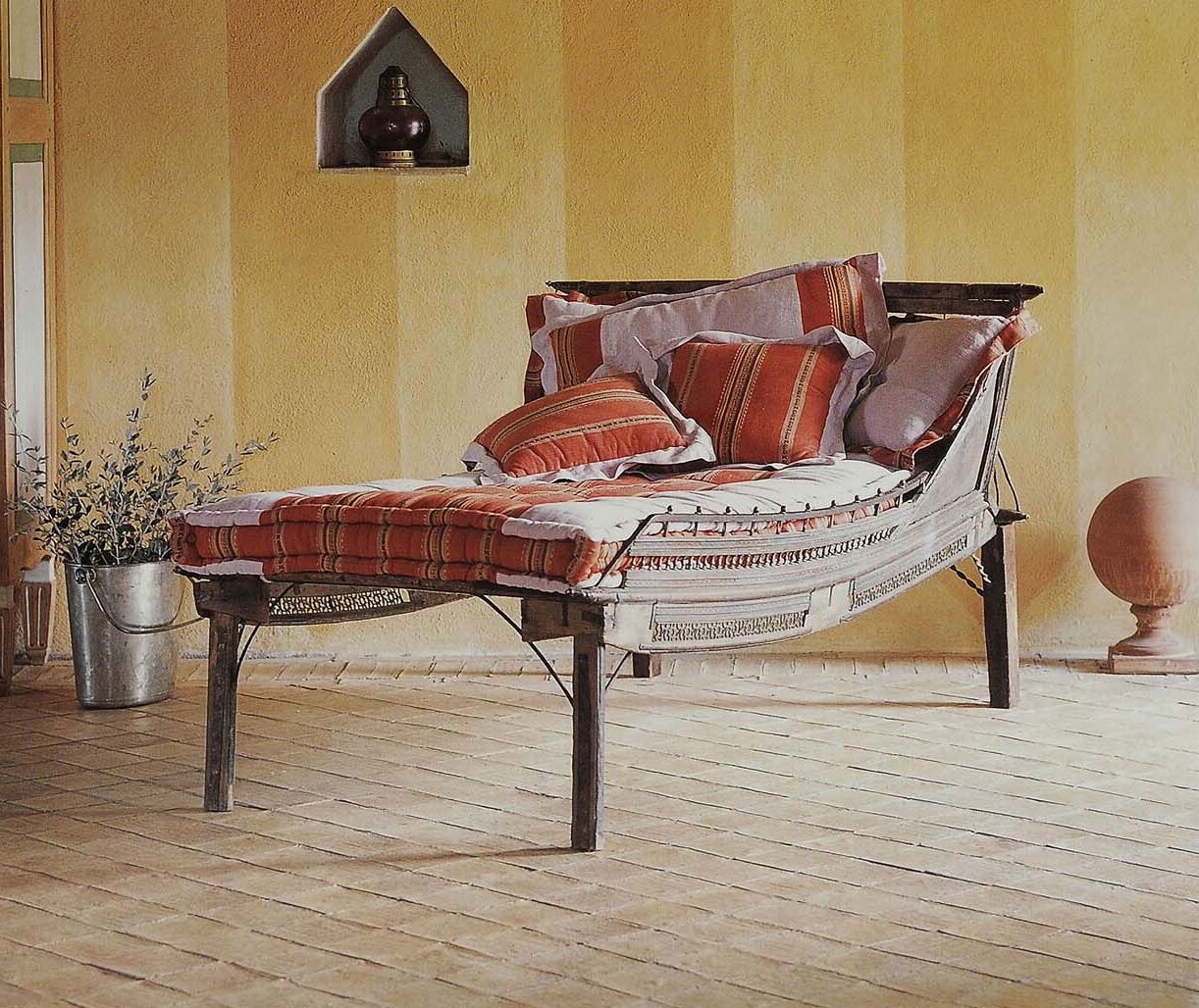 Un lit avec une couverture à rayures et des oreillers, une plante en pot et une lampe fixée au mur.
