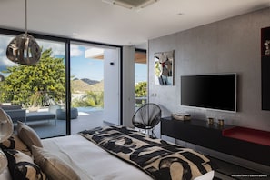 A modern bedroom with a large bed, a TV, and a view of the outdoors.