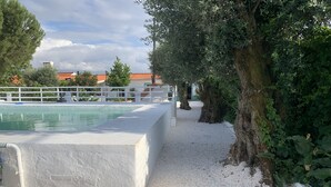 A swimming pool with a white deck, surrounded by trees and a white fence.