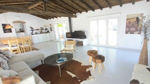 A spacious living area with a sofa, coffee table, and chairs, a television, and a kitchen in the background.