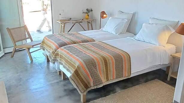 A bedroom with a bed, a chair, a small table, and a lamp.