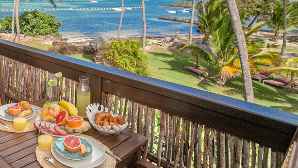 A balcony with a breakfast setup overlooking a beach and ocean.