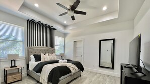 A modern bedroom with a large bed, a ceiling fan, a TV, and a mirror. - Scenic Retreat W/ Playground & Grilling (Granbury)