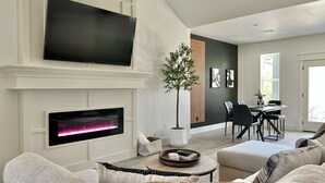 A modern living room with a fireplace, a flat-screen TV mounted above it, and a dining area in the background. - Scenic Retreat W/ Playground & Grilling (Granbury)
