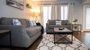 Un salon avec deux canapés gris, une table basse, un lampadaire et un tapis à motifs.