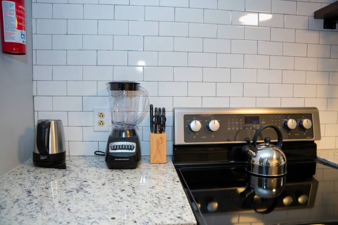 A kitchen with white tiled backsplash, a black stove, a kettle, a blender, and a coffee maker.