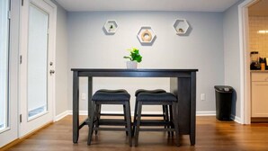 Une cuisine moderne avec une table en bois foncé et deux tabourets assortis, une plante en pot posée sur la table et des décorations murales hexagonales.
