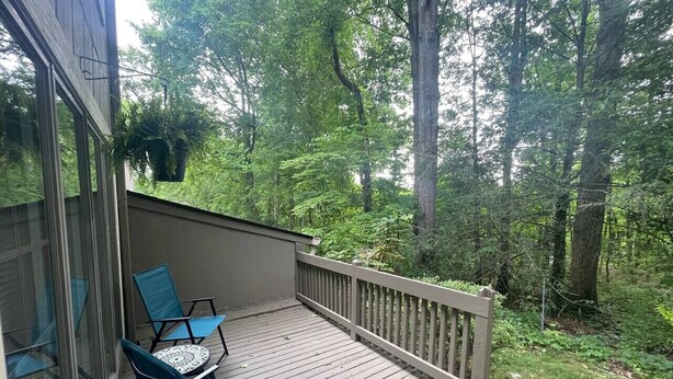 Une terrasse en bois avec deux chaises bleues et une table, entourée d’une balustrade en bois et d’une végétation luxuriante.