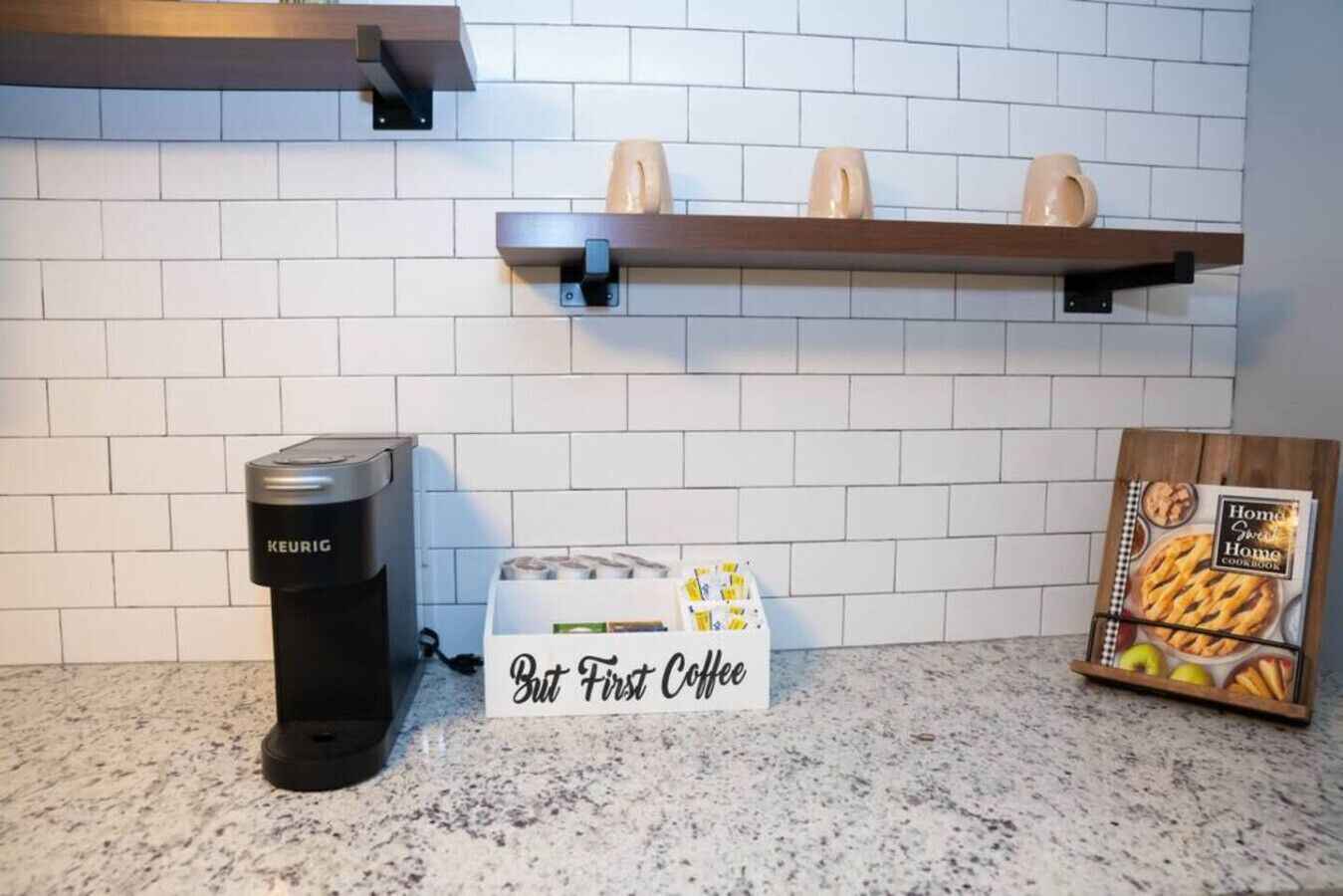A kitchen with a Keurig coffee maker, a box labeled "Bit First Coffee," and a cookbook on the counter.
