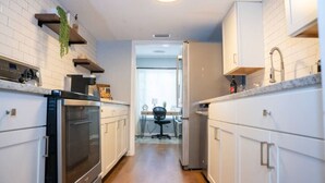Une cuisine étroite avec des meubles blancs, un four encastré et un plan de travail sur lequel se trouve une bouilloire.
