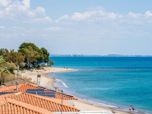 A coastal view with a beach, a clear sky, and solar panels on a building. - Dream vacation on the Mediterranean beach (Mont-roig del Camp)