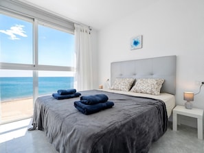 A bedroom with a large window overlooking the sea, a bed with grey bedding, two pillows, and a bedside table with a lamp. - Dream vacation on the Mediterranean beach (Mont-roig del Camp)