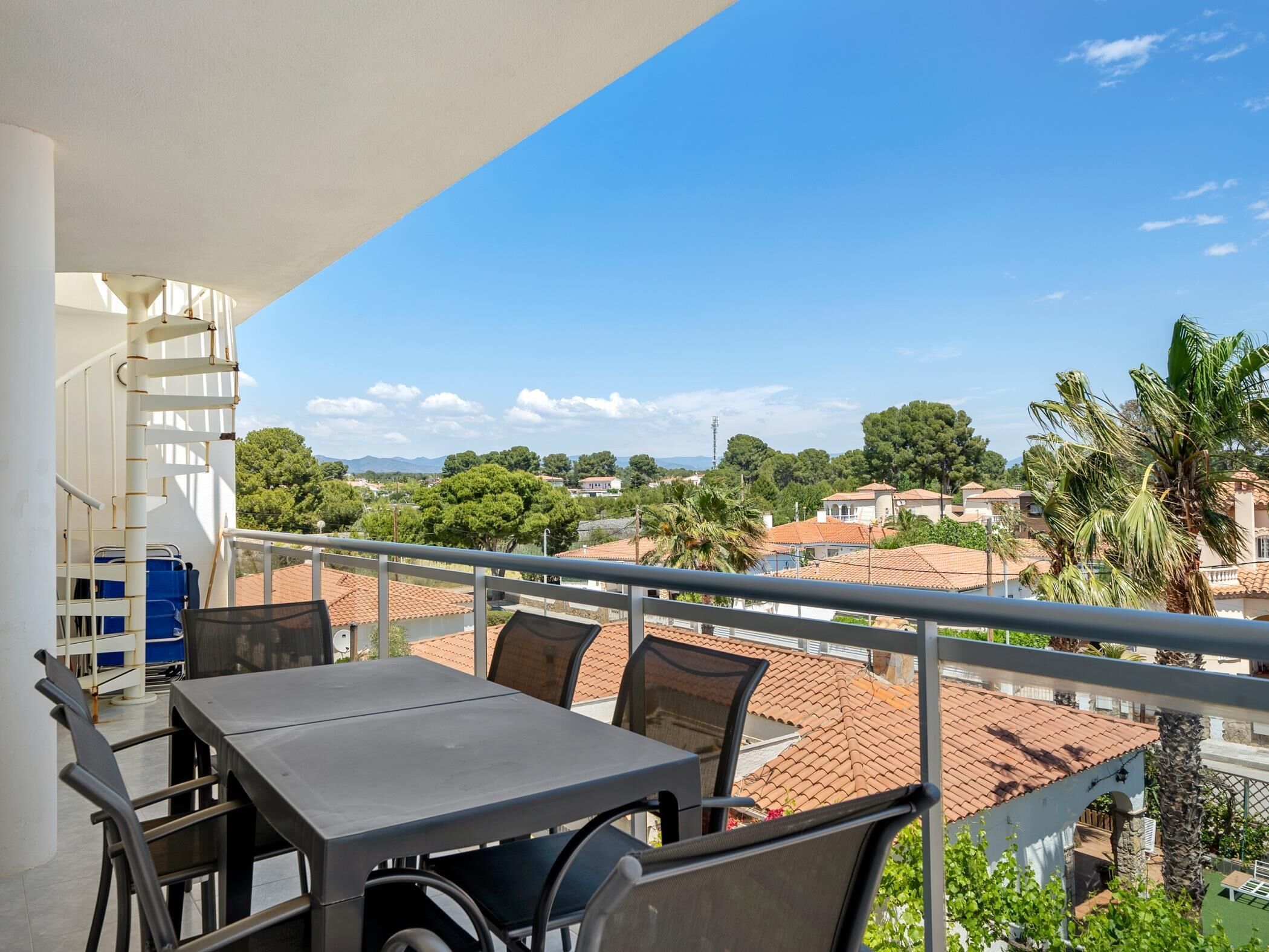 Een balkon met een tafel en stoelen, met uitzicht op een woonwijk met huizen en bomen.