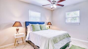A bedroom with a bed, two bedside tables, a ceiling fan, and two windows with blinds.