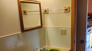 A bathroom with a green sink, a toilet, a mirror, and wall-mounted lights.