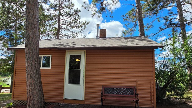 A small cabin with a front door, a bench, and a chimney.