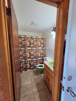 A bathroom with a shower curtain featuring a nautical theme, a green toilet, and wooden cabinetry. - East Crooked Lake Cabin 3 (Nevis)