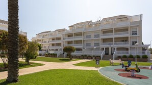 Um hotel com vários andares, varandas, um parquinho e um gramado bem cuidado.