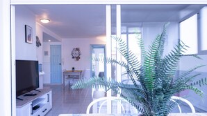 A modern living room with a television, dining table, chairs, and a potted fern.