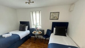 A hotel room with two single beds, a small table with a vase and two cups, a chair, and a window with blinds. - Remarkable Studio flat in Cambridge (Cambridge)
