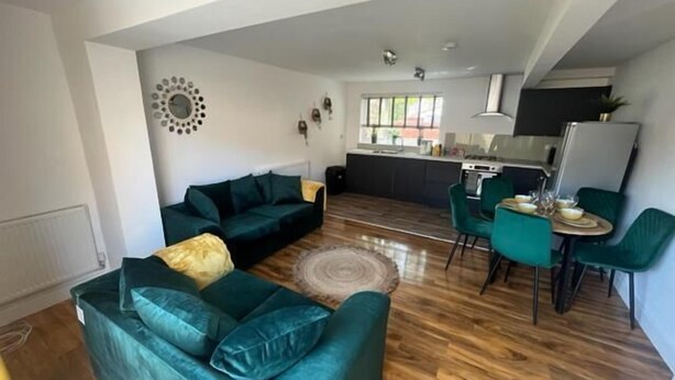 Un salon moderne avec un canapé vert, un coin repas avec des chaises turquoise et une cuisine en arrière-plan.