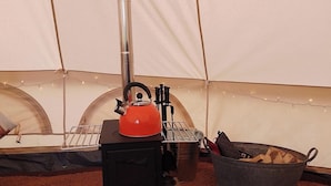 L’intérieur d’une tente, avec un réchaud portable, une bouilloire et un seau de bois de chauffage.