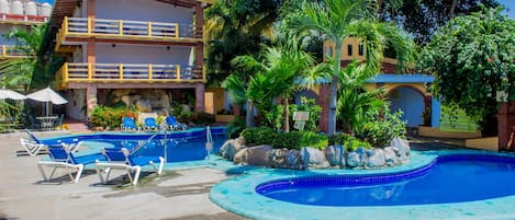 A pool area with lounge chairs, a building with a balcony, and tropical vegetation.