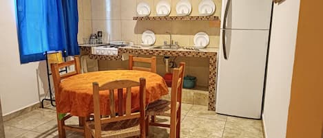 Una cocina compacta con una mesa redonda, sillas de madera, una estufa y un refrigerador.
