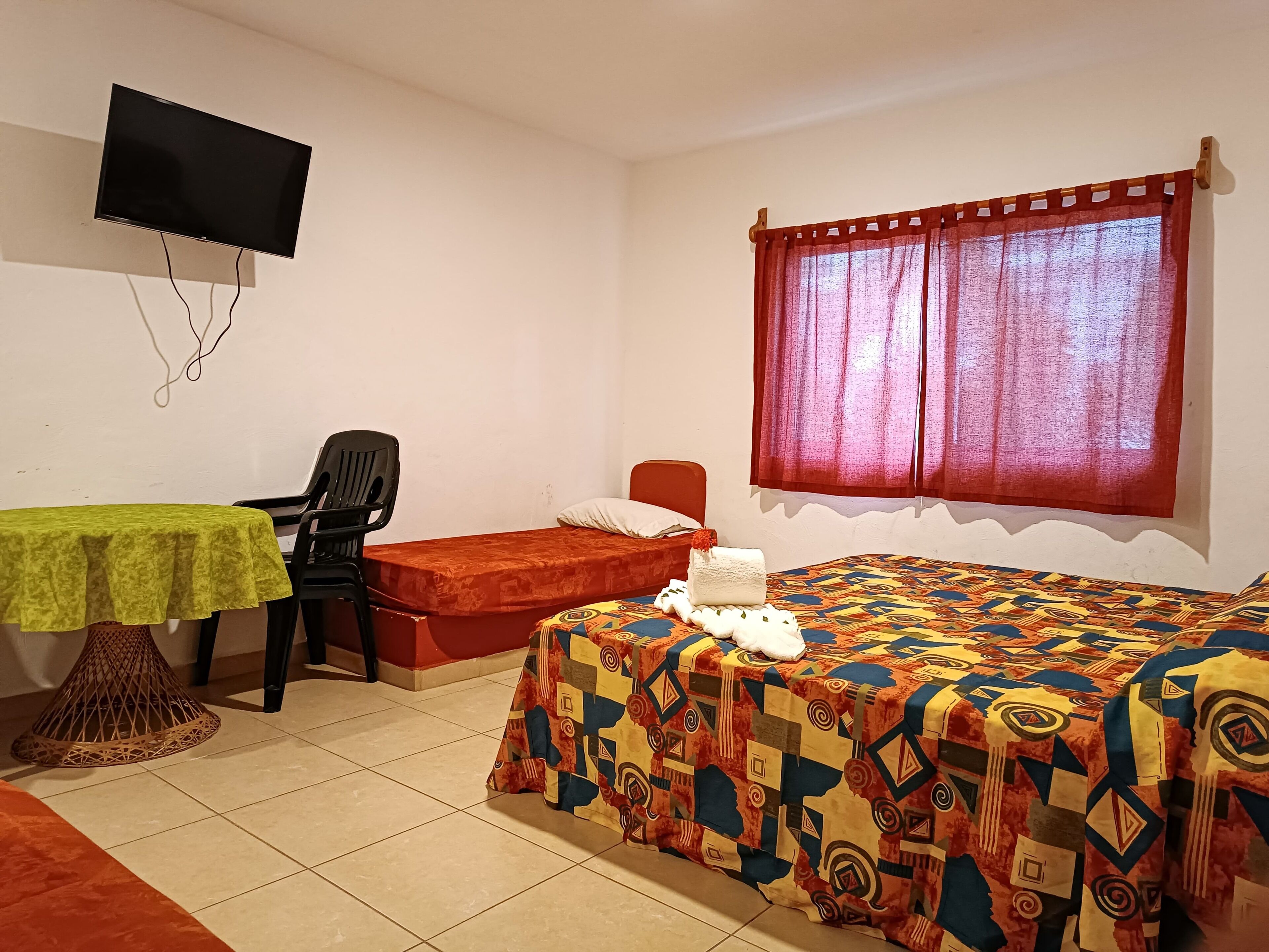 A room with a bed, a desk with a chair, a television mounted on the wall, and a window with curtains.