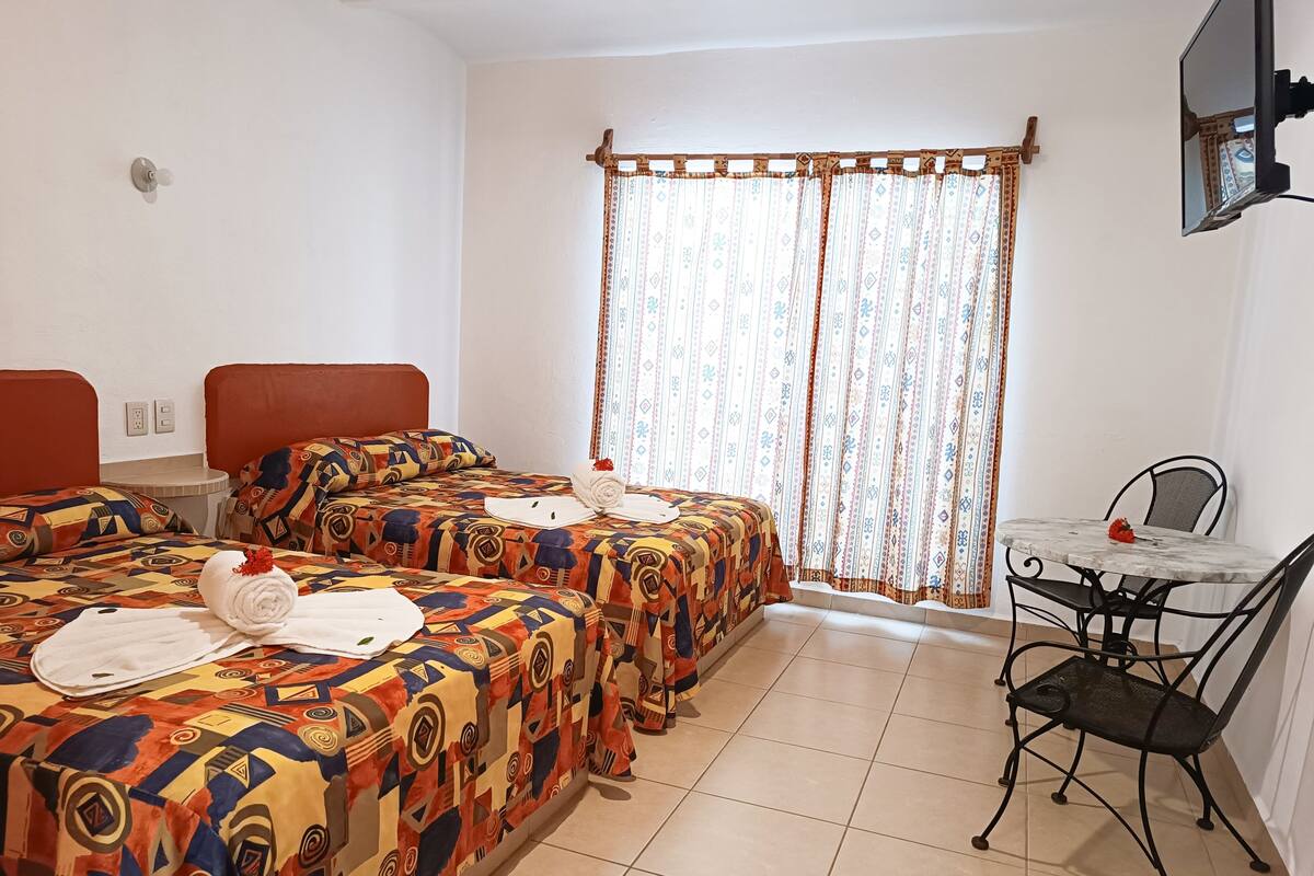 Une chambre d’hôtel avec deux lits, une petite table, une chaise et un téléviseur fixé au mur.
