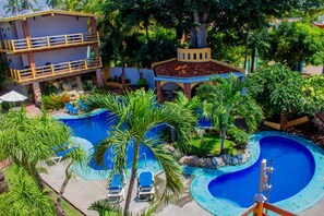 A resort with a swimming pool, palm trees, and a multi-story building with balconies.