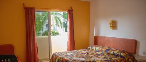 A room with a bed, a chair, a table, and a sliding door to a balcony.