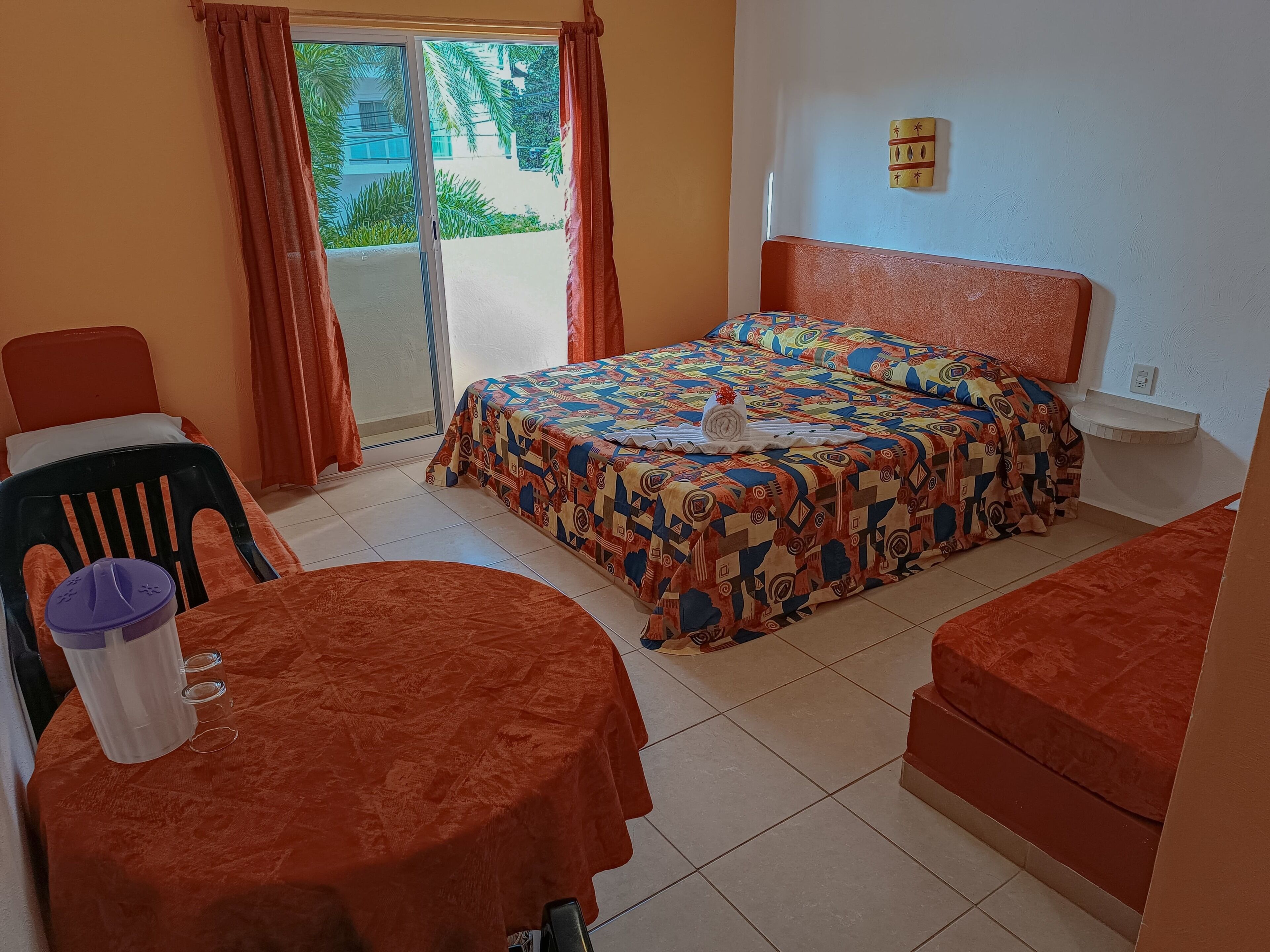 Una habitación de hotel con una cama, una mesita con una silla, un sofá y una ventana con cortinas.
