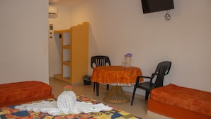 Una habitación pequeña con una cama, una mesa y dos sillas, un televisor en la pared y una escalera al fondo.