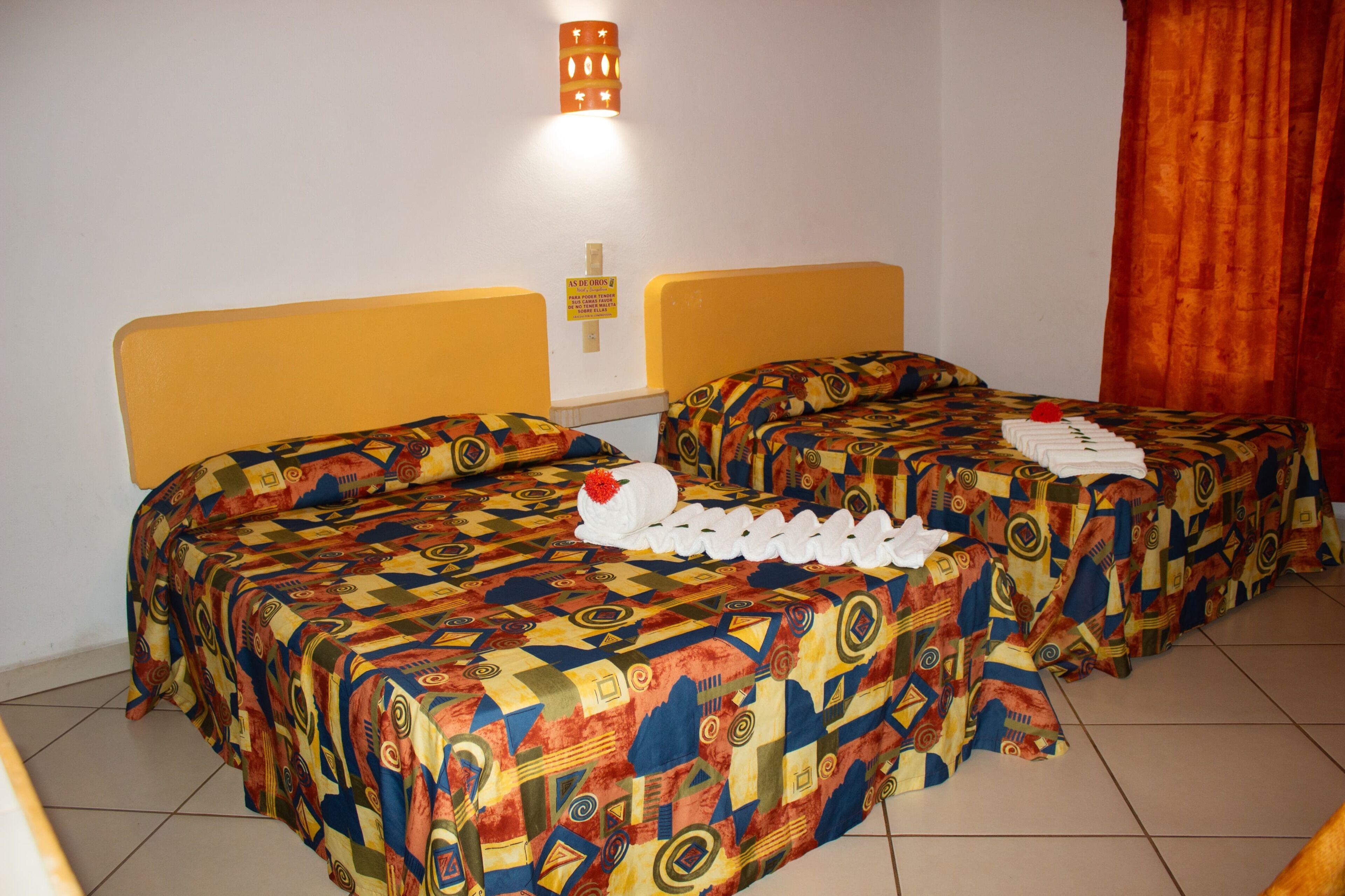 Une chambre d'hôtel avec deux lits, chacun recouvert d'une courtepointe aux motifs colorés et agrémenté d'oreillers blancs.