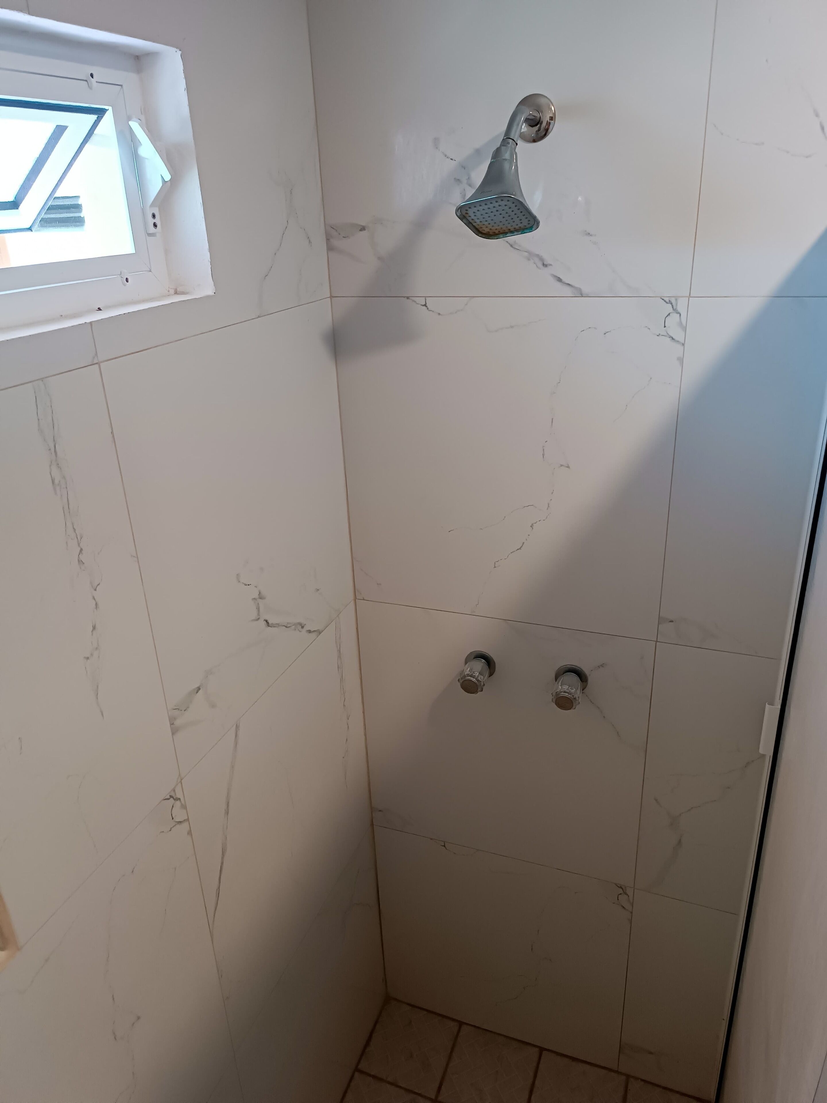A shower with a handheld showerhead and a window above it.