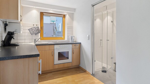 Une cuisine compacte dotée d’un four encastré, d’une fenêtre au-dessus de l’évier et d’une porte-fenêtre coulissante donnant sur un espace douche.