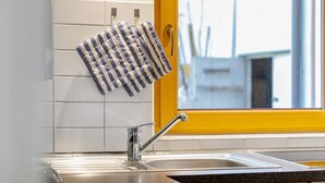 Une cuisine avec un évier en acier inoxydable, une fenêtre avec un cadre jaune et une serviette suspendue à un porte-serviettes.