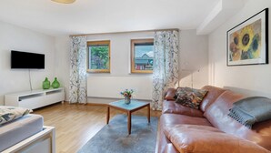 Un salon moderne avec un canapé, une table basse, un téléviseur et une fenêtre avec des rideaux.
