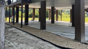 A covered outdoor area with a concrete floor, supported by multiple pillars, and a metal railing along the upper edge. - New riverfront home across from Rock Bluff Springs on the Suwannee river (Branford)