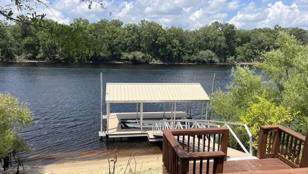 A wooden deck with a view of a dock and a boat. - New riverfront home across from Rock Bluff Springs on the Suwannee river (Branford)