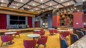 A restaurant with round tables and red chairs, a stage with musical instruments, and a bar area with shelves of bottles. - King Room at a 4⭐️ Hotel (Nashville)