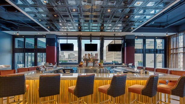 Een moderne barruimte met een hoge plafond, grote ramen en meerdere schermen.