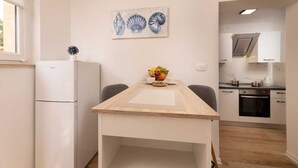 Eine kompakte Küche mit Kühlschrank, einem Esstisch mit Stühlen und einer Wanddekoration mit Muscheln.