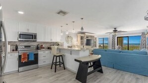 Una cocina moderna con armarios blancos, electrodomésticos de acero inoxidable y un sofá azul en la zona de estar.