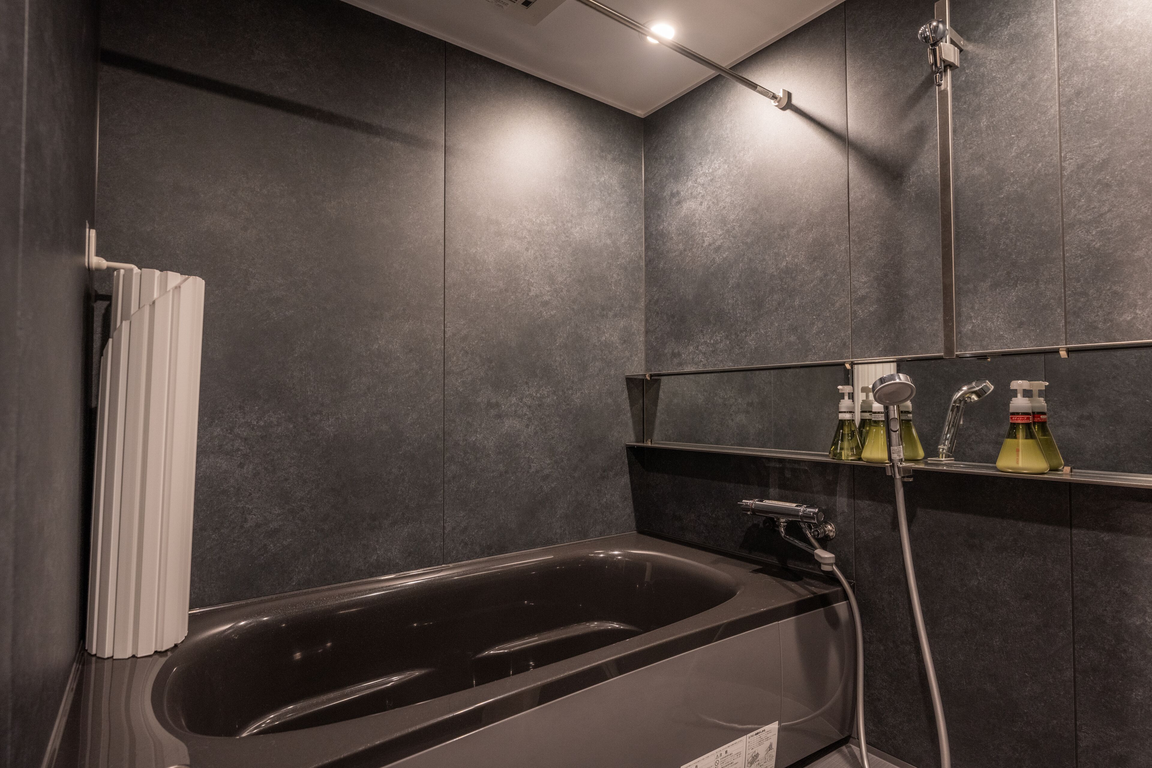 A modern bathroom with a black bathtub, a shower, and a shelf with toiletries.